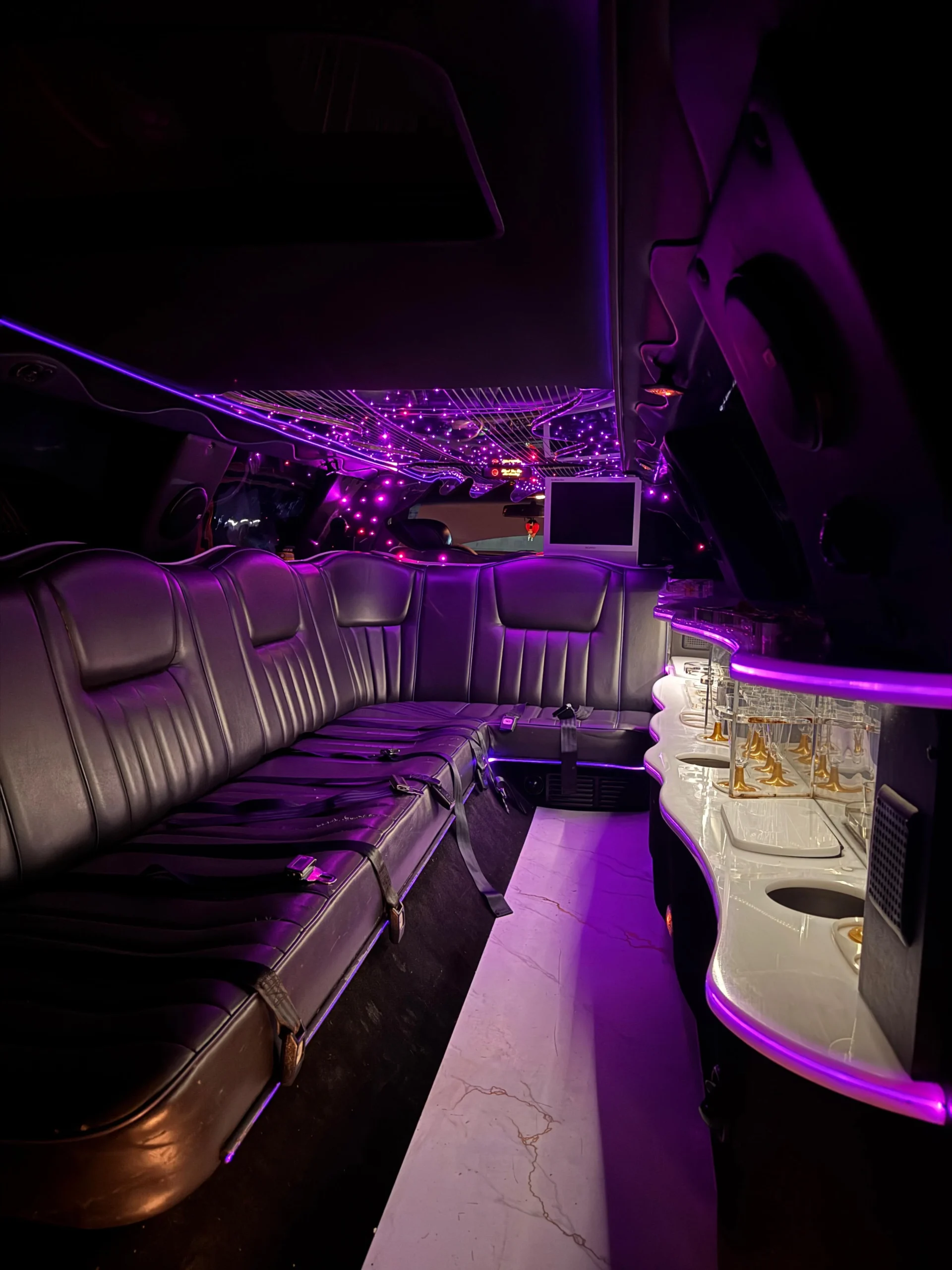 Interior de limusina Lincoln americana blanca con elegante iluminación color lila, ideal para eventos y alquiler de limusinas en Barcelona