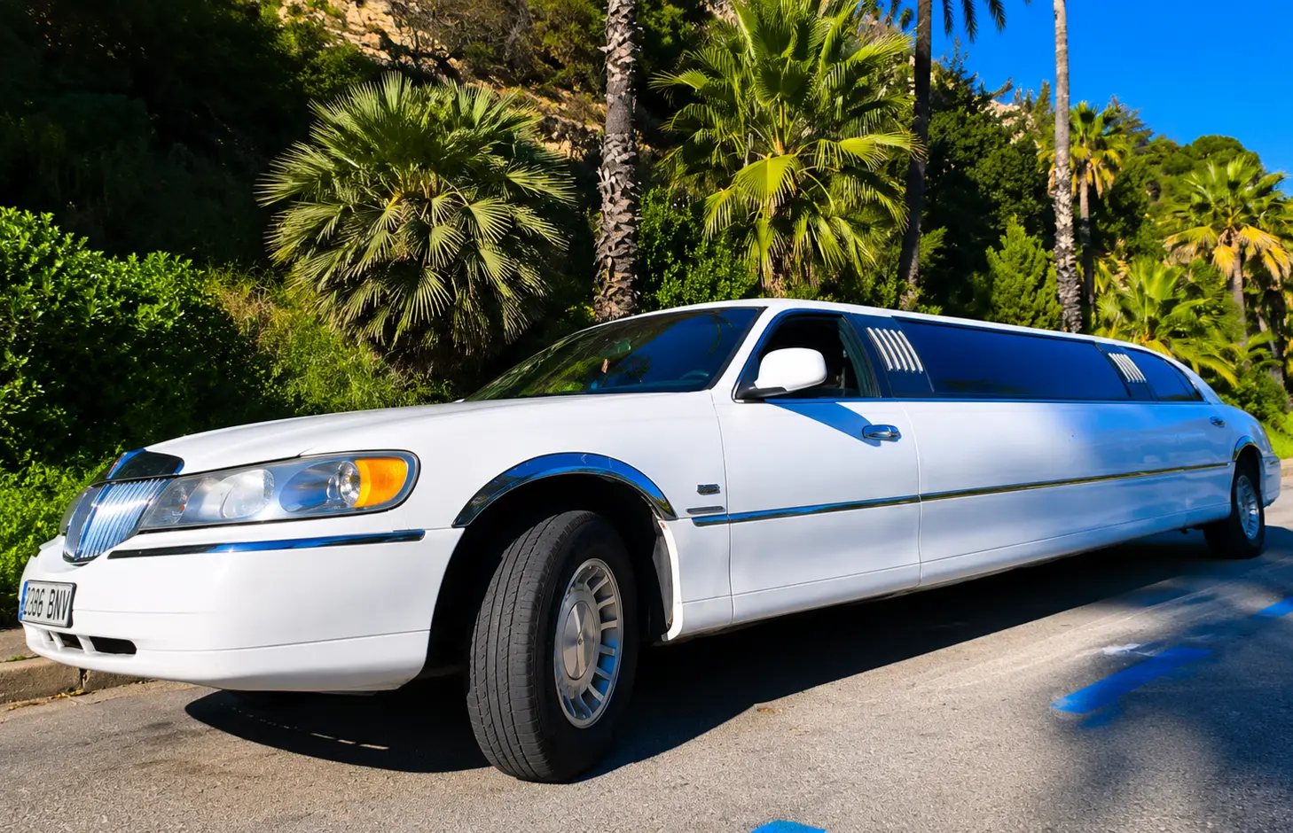 white lincoln limousine White Lincoln stretch limousine in Barcelona, Spain, featuring tinted windows, chrome accents, and a tropical-style landscape on a sunny day.